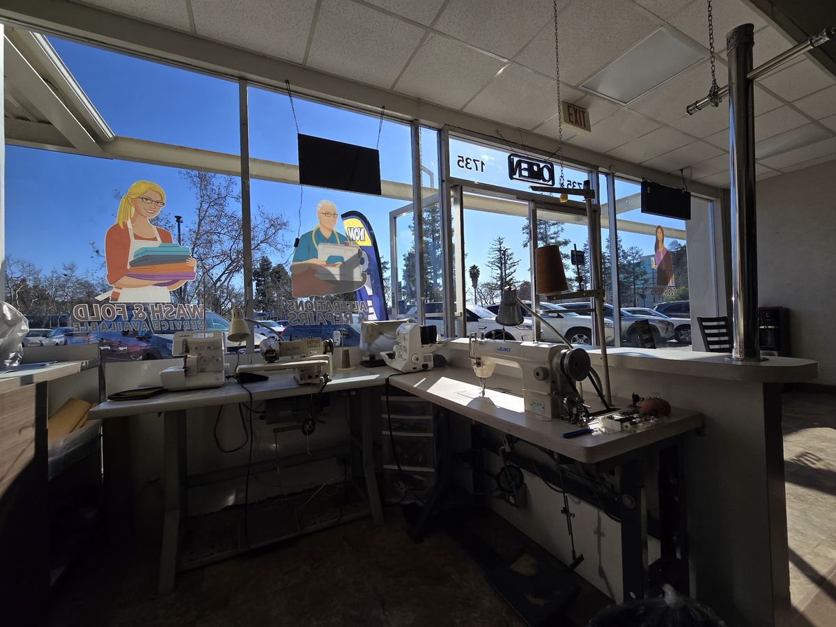 Sewing machines and alteration work tables lined up along the shop’s front windows