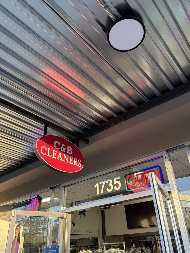 Red oval C&B Cleaners sign hanging under the walkway awning above the open front door, with 1735 and an OPEN sign in the window