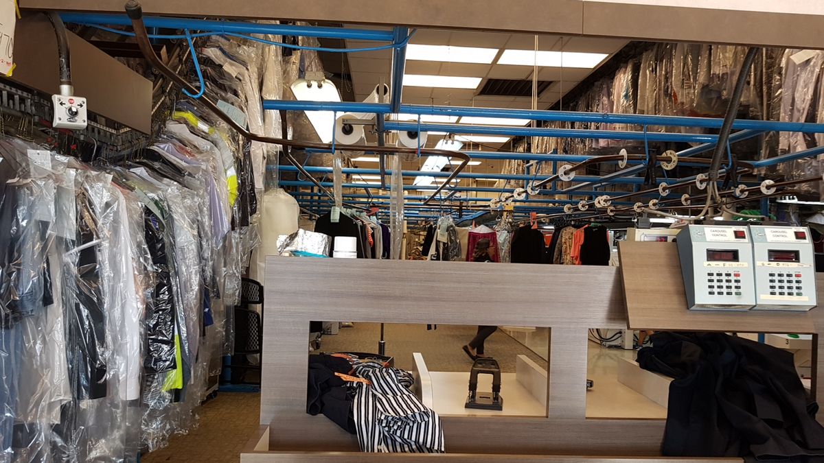 Rows of cleaned garments in plastic bags on the motorized conveyor behind the C&B Cleaners counter