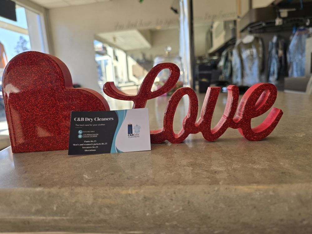 A C&B Dry Cleaners business card propped against red glitter heart and Love decorations on the counter